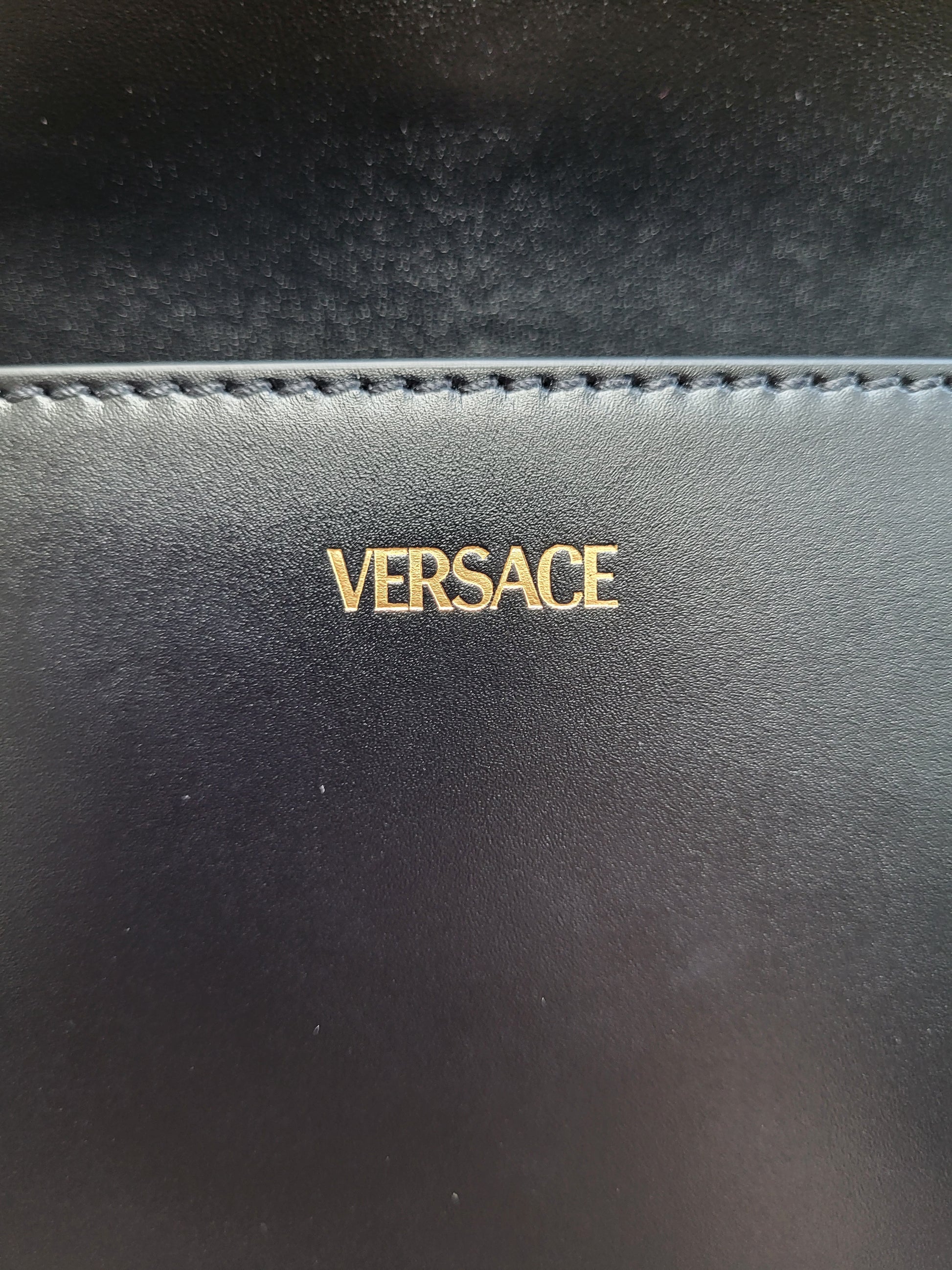 Black leather product with 'Versace' logo in gold on a dark background
