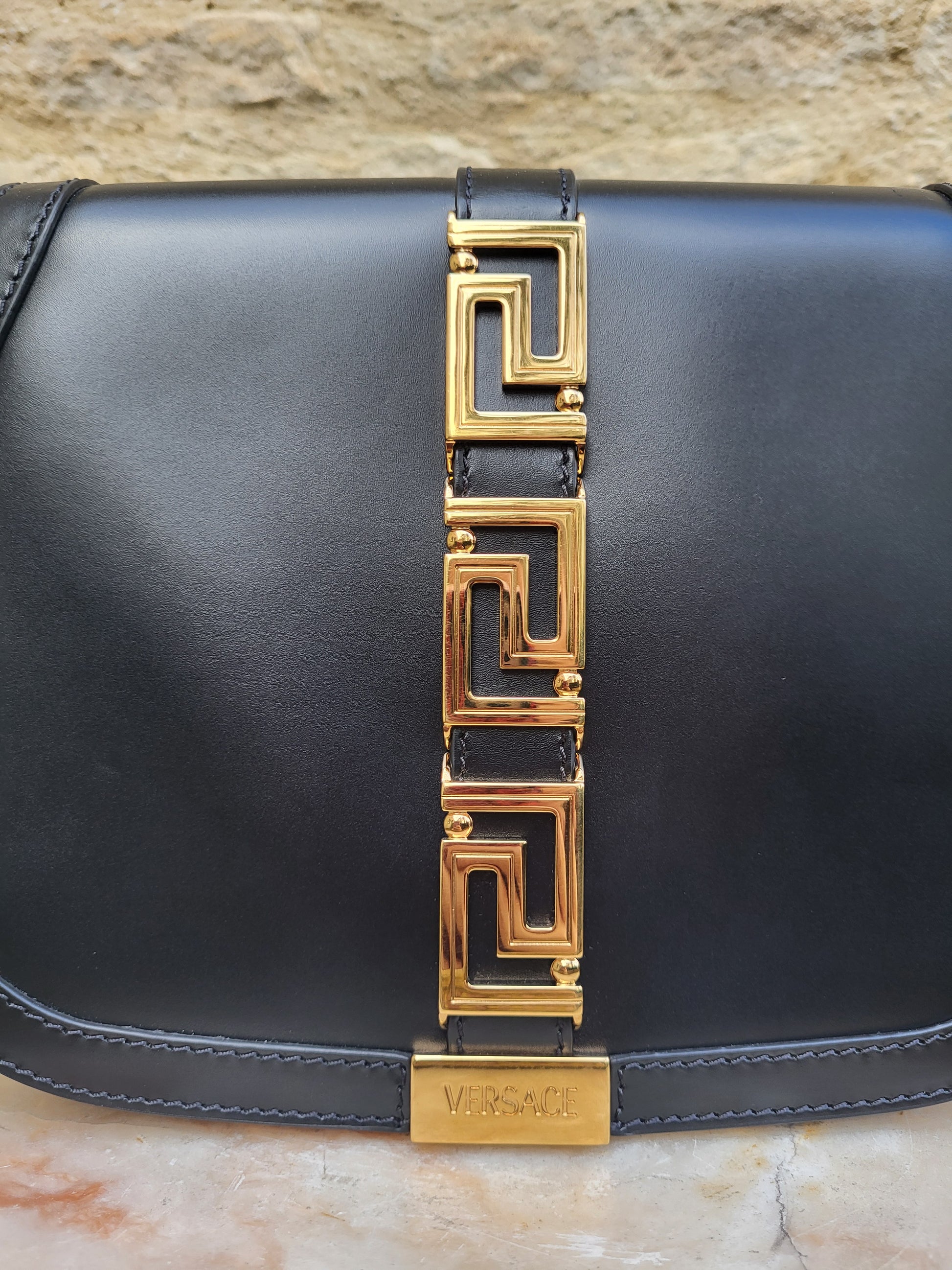 Versace Greca Goddess black leather crossbody bag, brand new with tags. Close up of Versace logo.